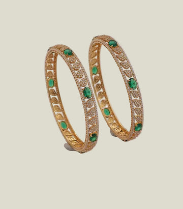 Pair of gold bangles with green gemstones on a light background