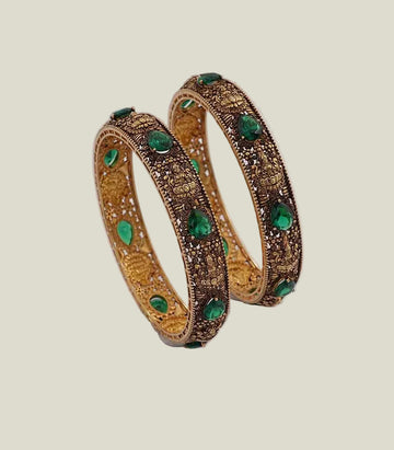 Pair of gold bangles with green gemstones on a white background