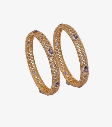 Pair of gold bangles with purple stones on a light background